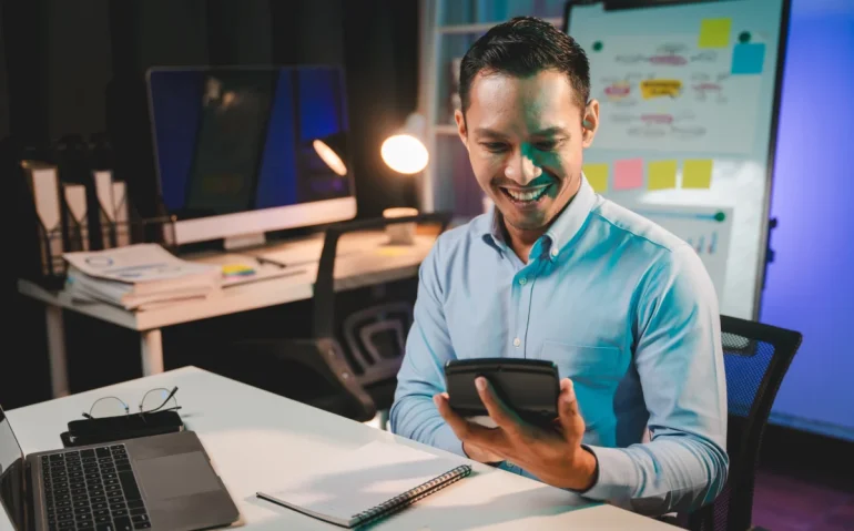 man-smiles-using-calculator-at-desk